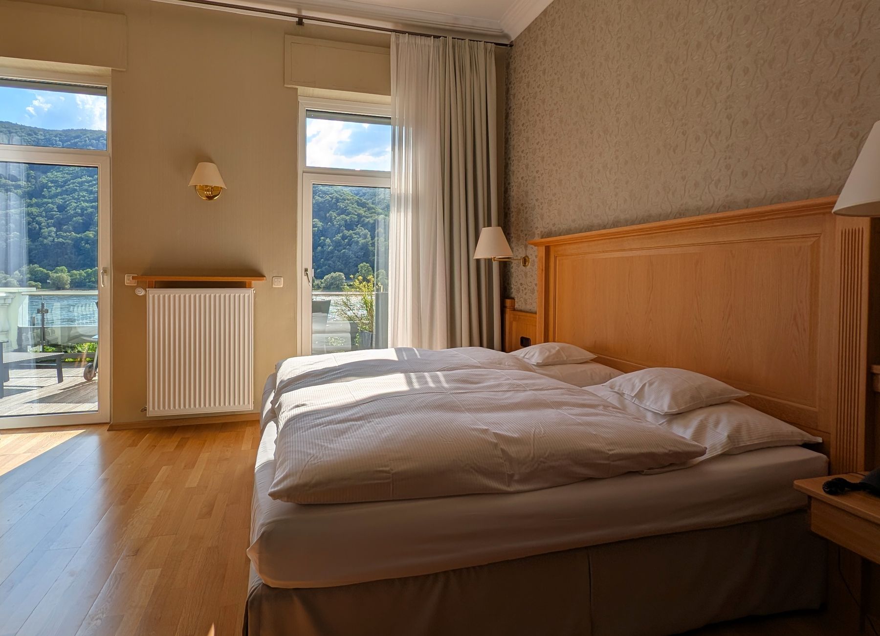 Doppelbett auf Parkett, daneben Fenster und Balkontür mit Blick auf den Hang