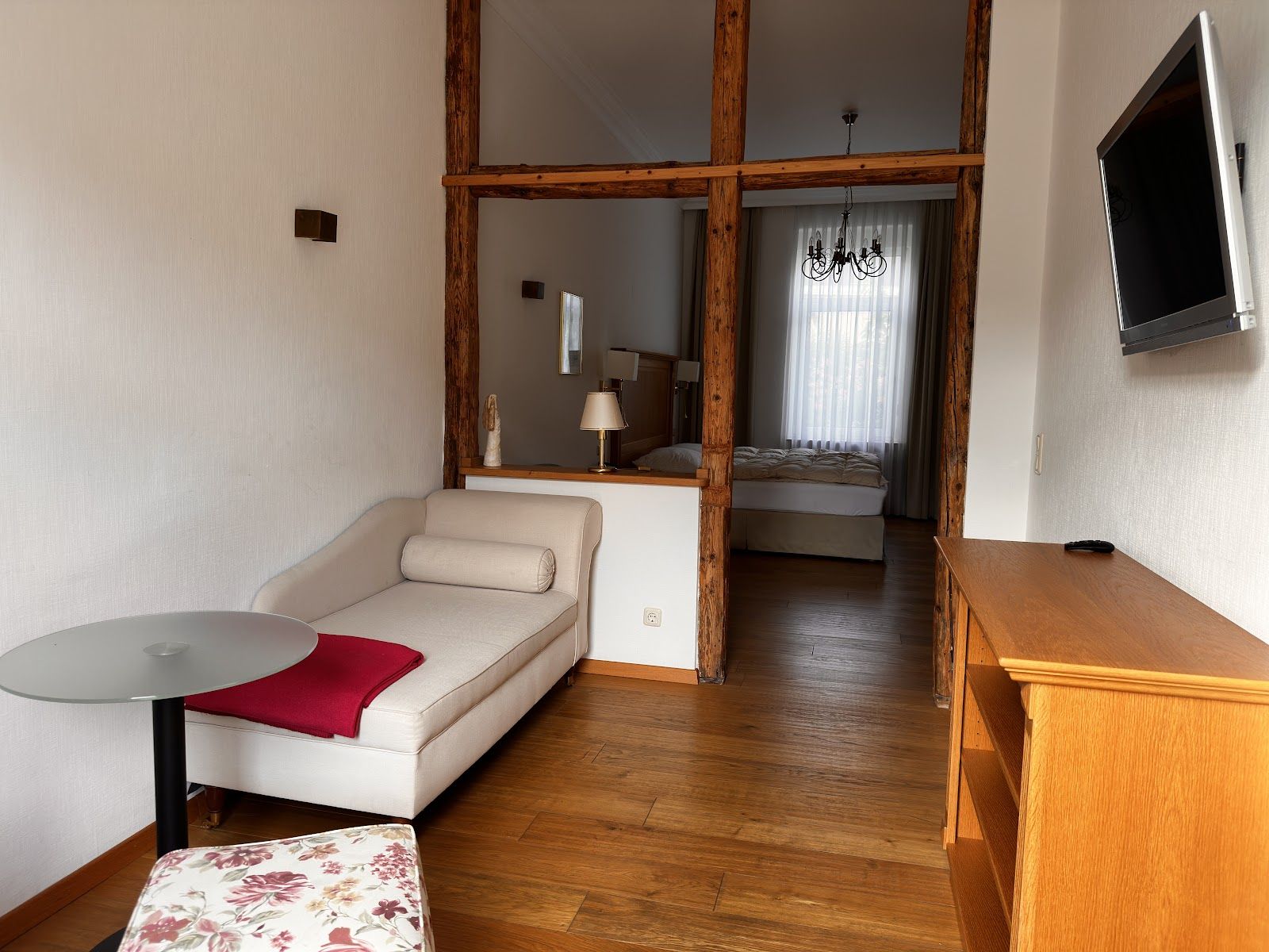 Wohnbereich mit Chaiselongue, dahinter durch ein offenes Holzgebälk der Schlafbereich mit Doppelbett