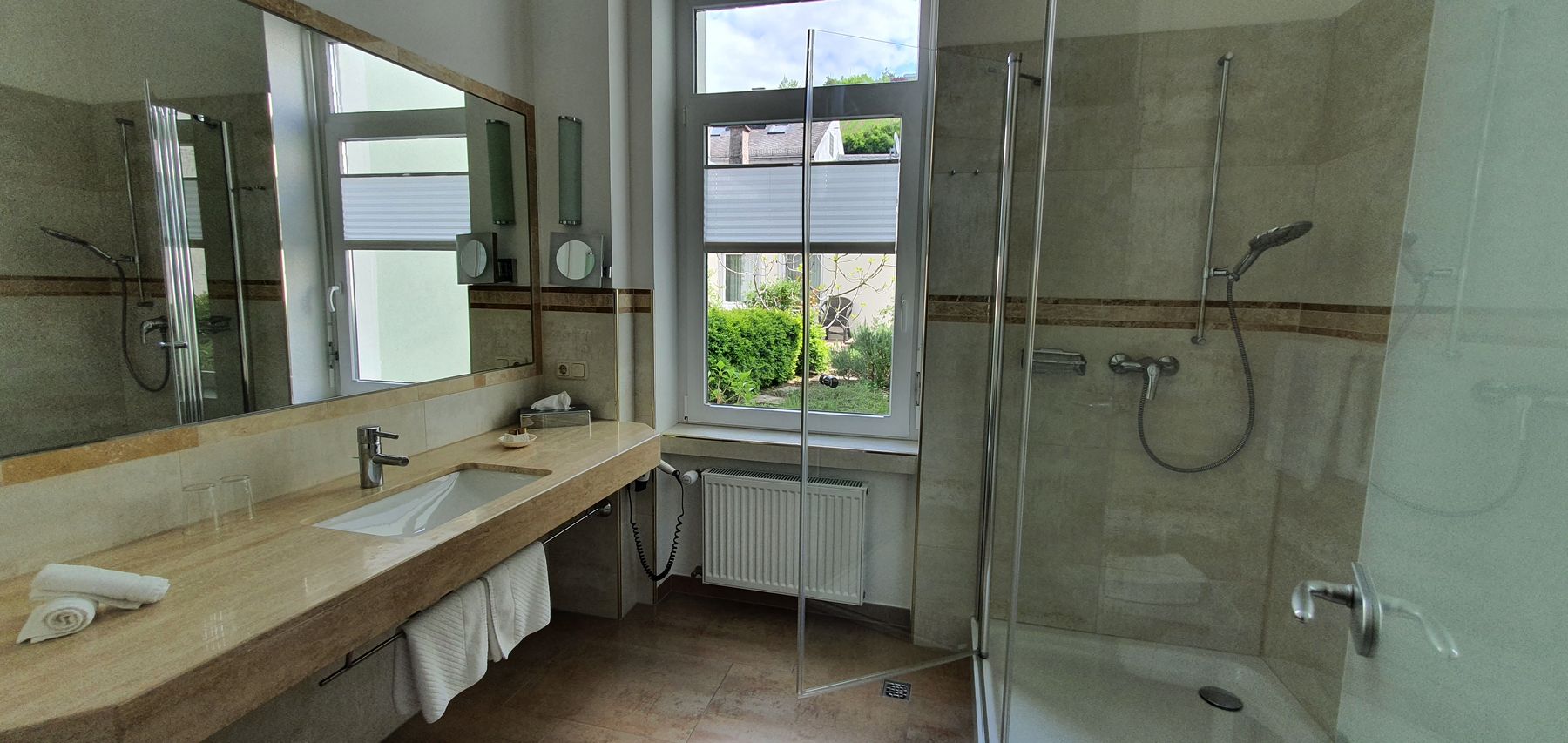 Bad der Deluxe Suite mit langem Waschtisch, großem Spiegel und gläserner Dusche am Fenster