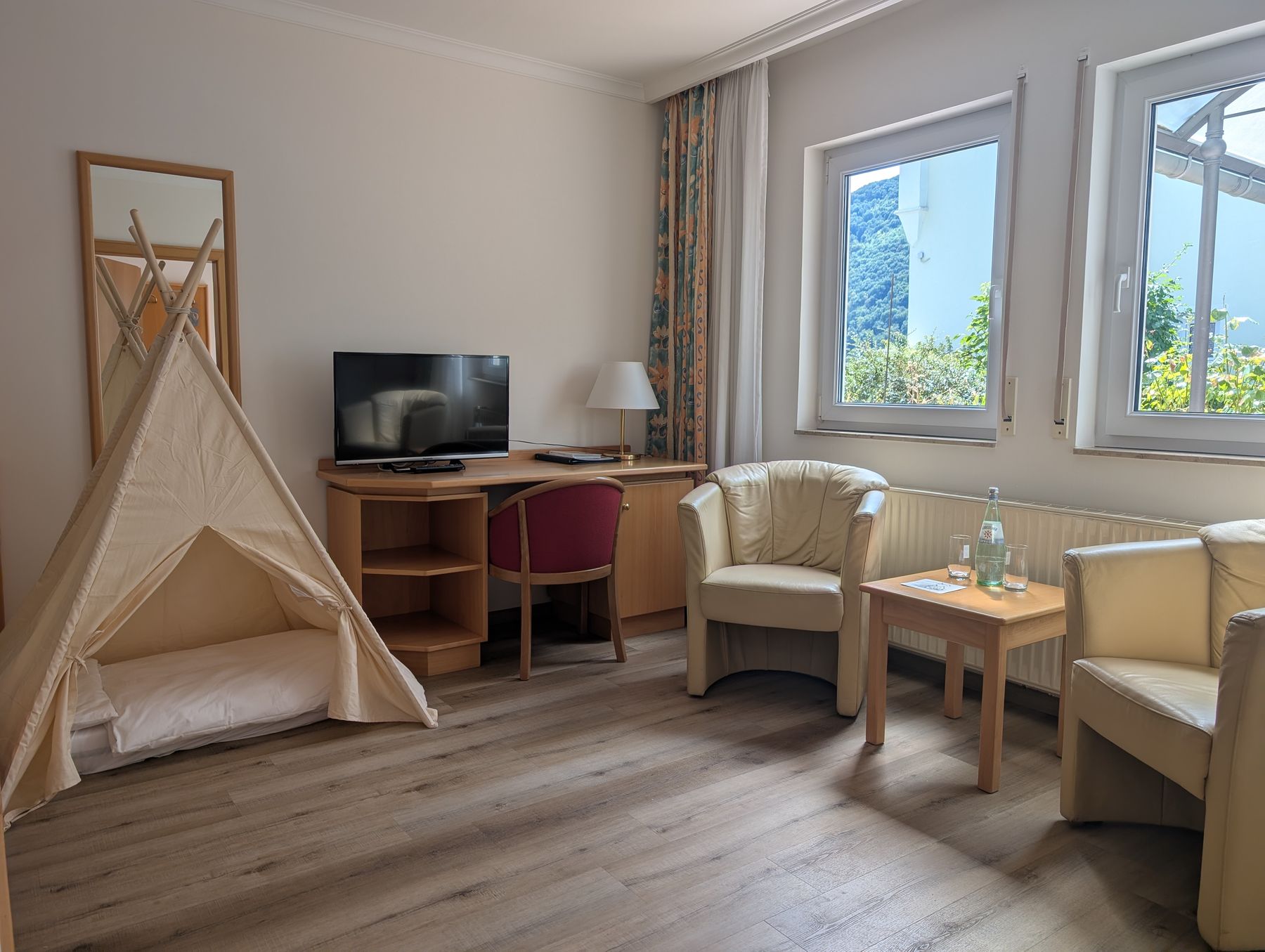 Familienzimmer mit Spielzelt, zwei Sesseln, Schreibtisch, Fernseher und Fenstern zum Grünen