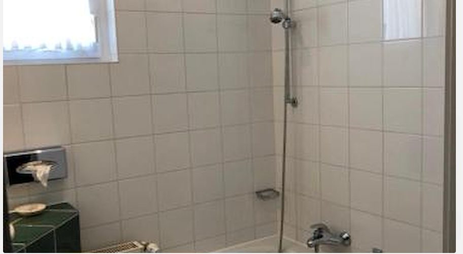 Badewanne mit Duschstange und hellen Fliesen